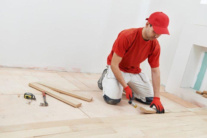 carpenter worker installing wood parquet board during flooring w