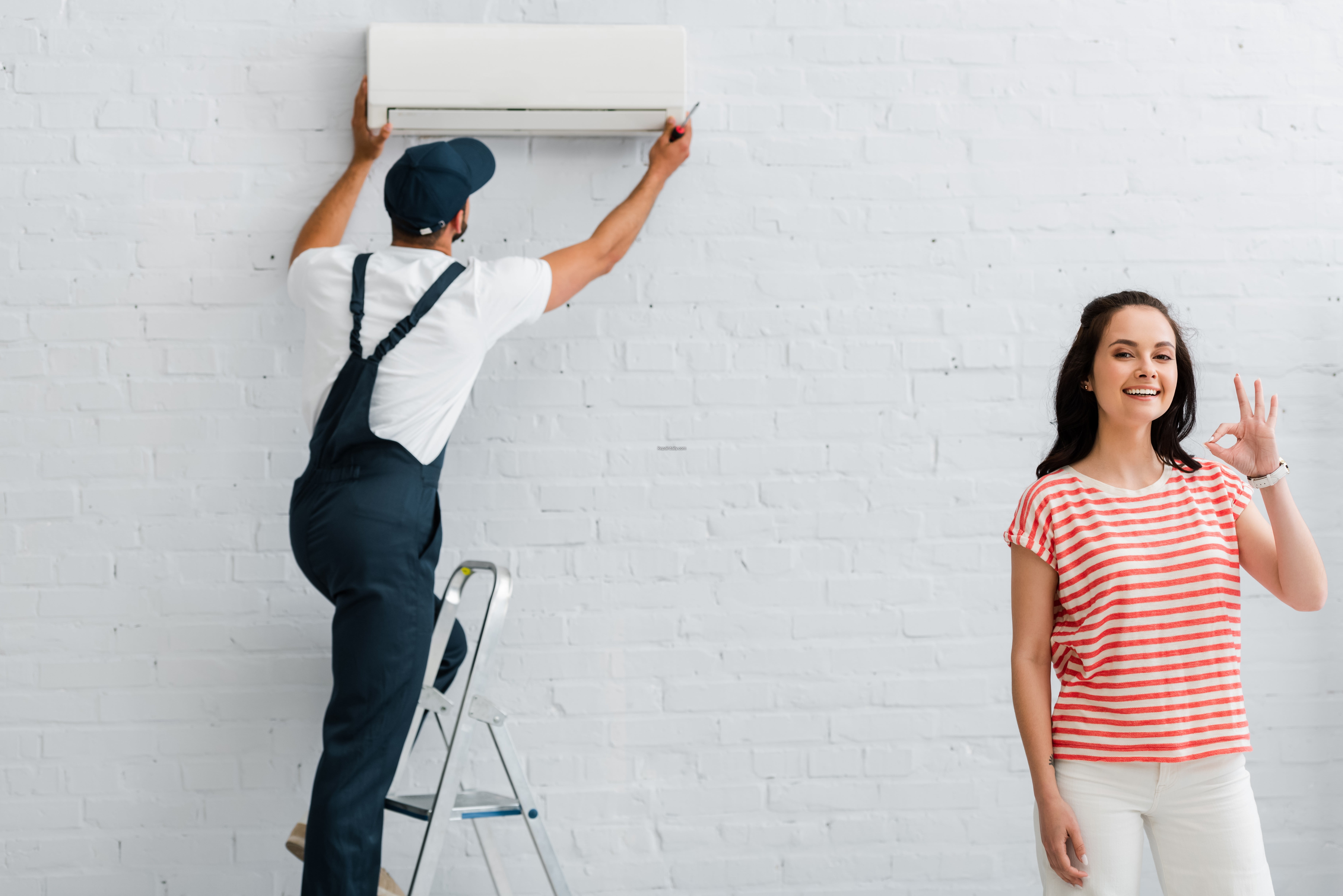 Smiling woman showing ok gesture while repairman fixing air cond