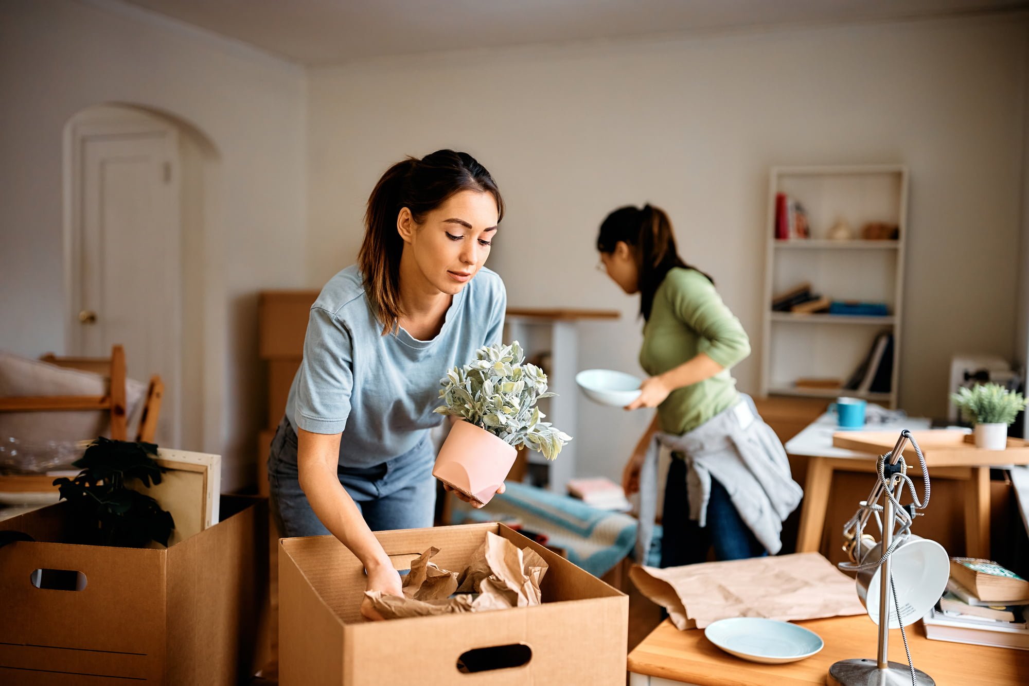 Young woman and her friend packing their belongings while preparing to move out of apartment.